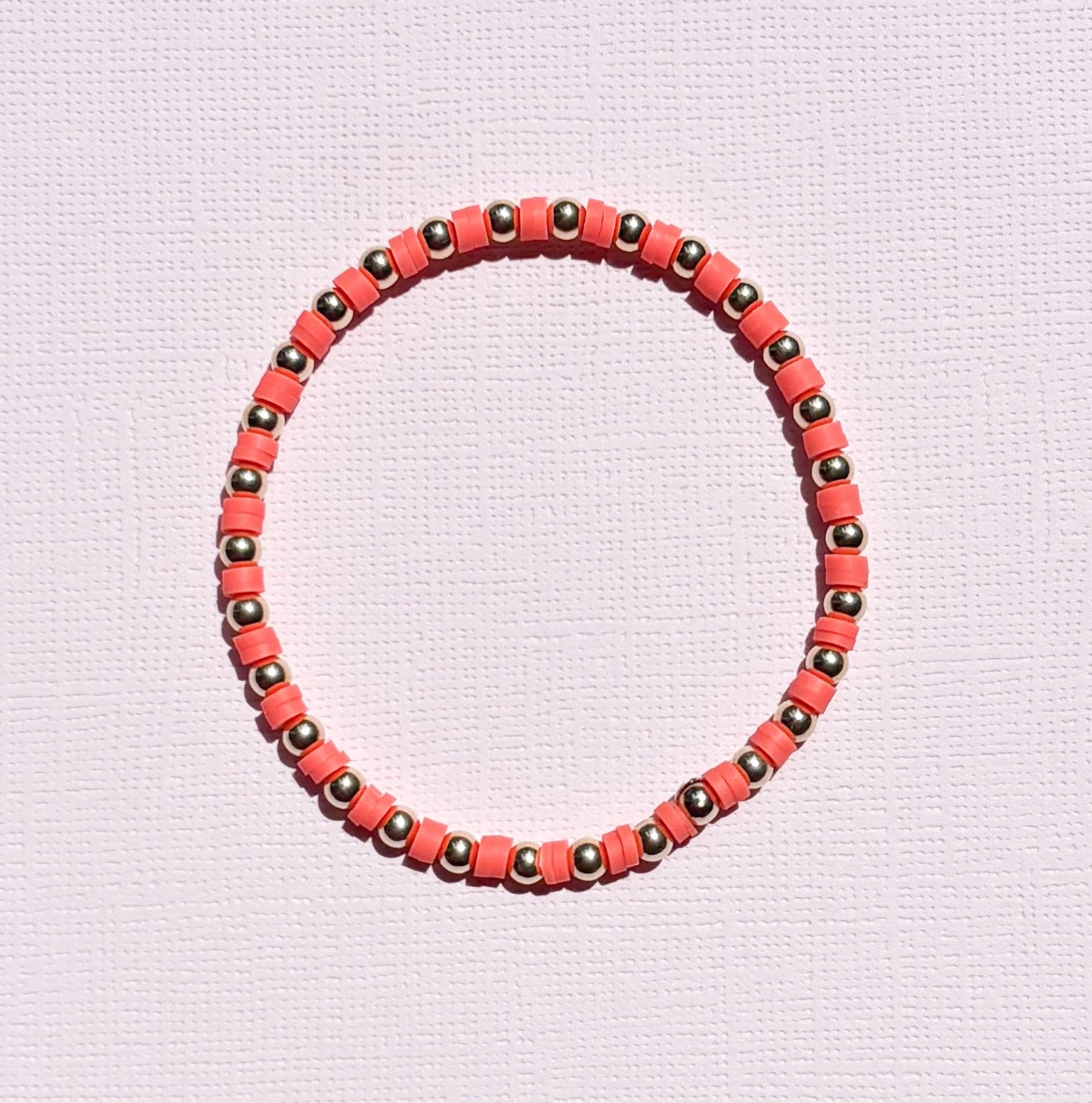 Bracelet with orange and gold beads on a light pink background